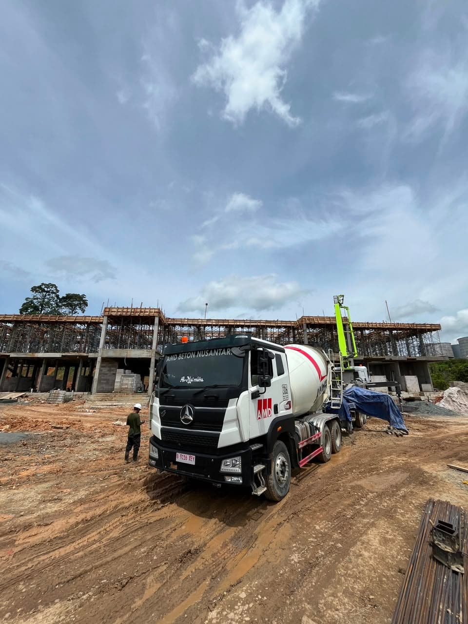 Truk pengaduk semen AMD Beton Nusantara di lokasi proyek konstruksi bangunan dengan tanah berlumpur.
